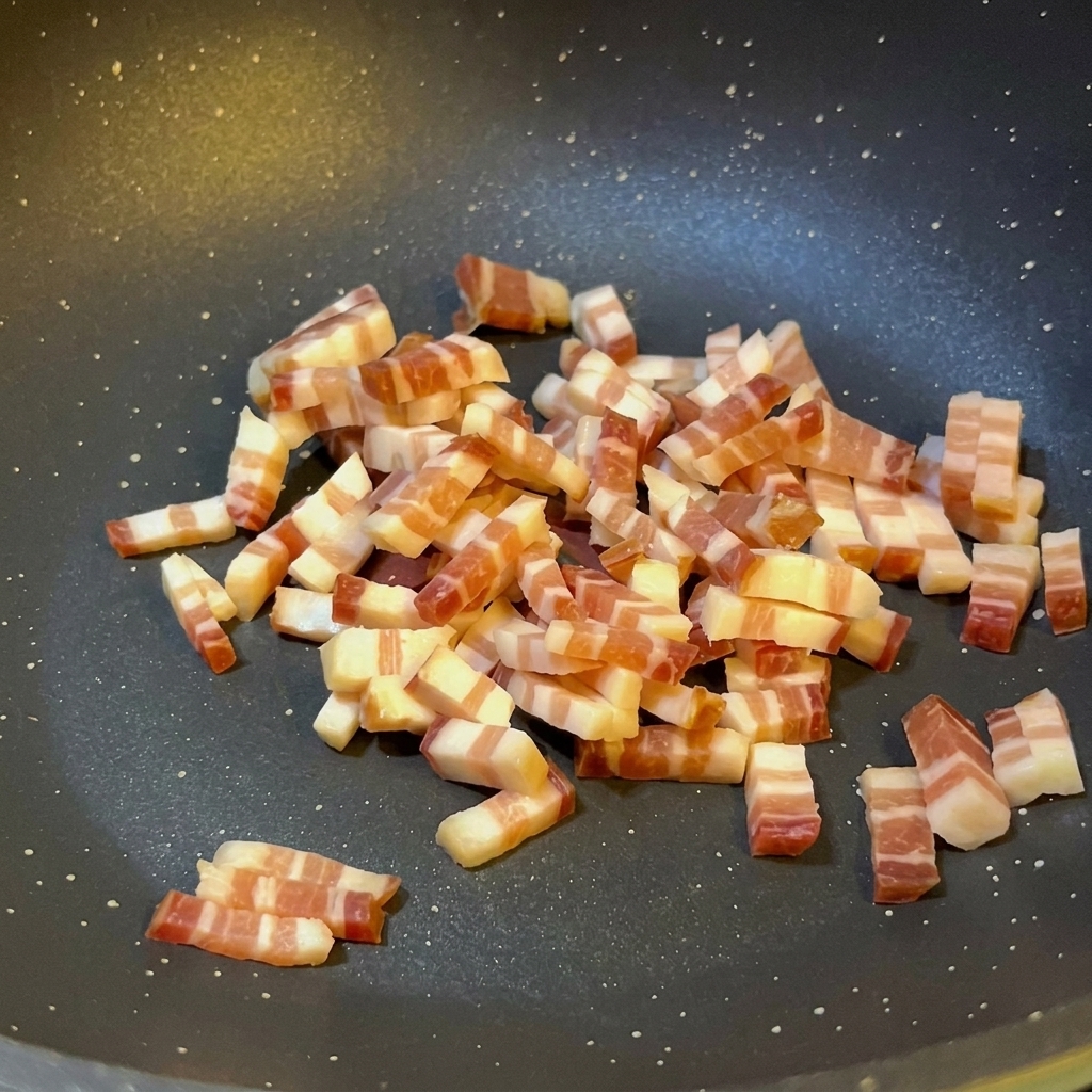 Kleine Würfel italienischer Pancetta braten in einer dunklen, beschichteten Pfanne und geben Fett ab.