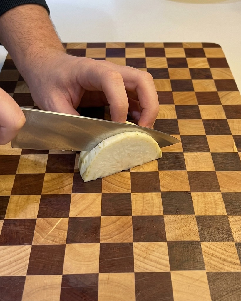 Eine Person schneidet eine weiße Zwiebel mit einem Kochmesser auf einem Holzbrett in feine Würfel.