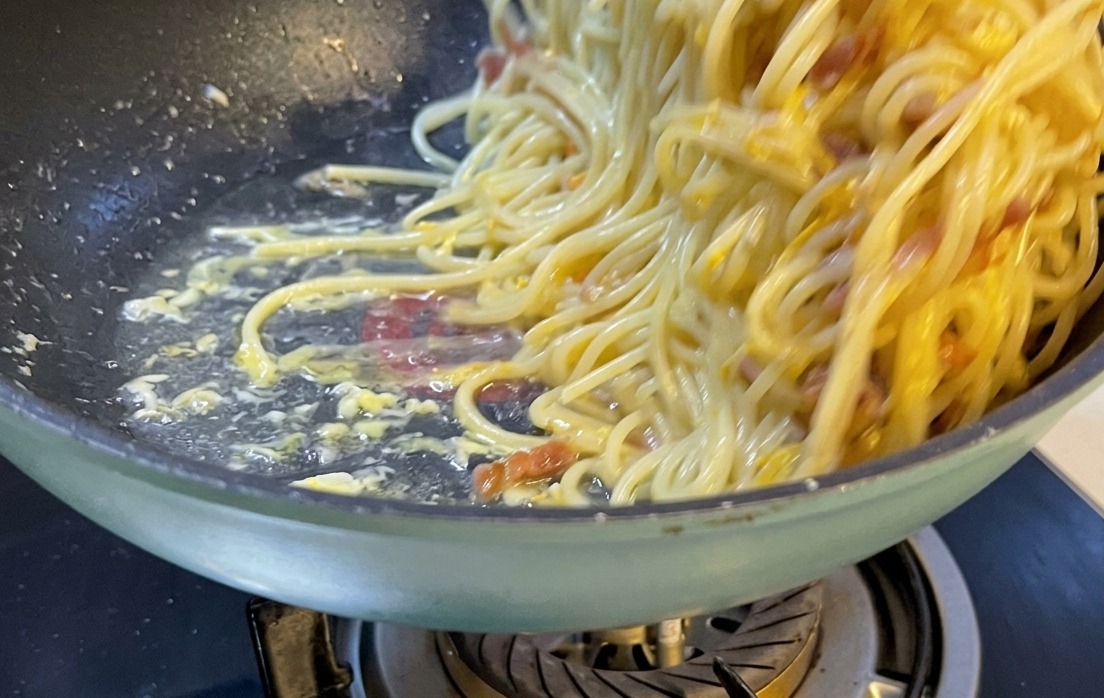 Eine wunderschön angerichtete Portion Spaghetti Carbonara auf einem weißen Keramikteller, garniert mit geriebenem Käse und Pfeffer.