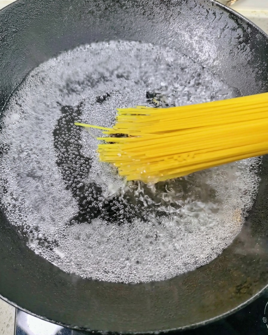 Trockene Spaghetti werden in einen Topf mit sprudelnd kochendem Wasser gegeben.