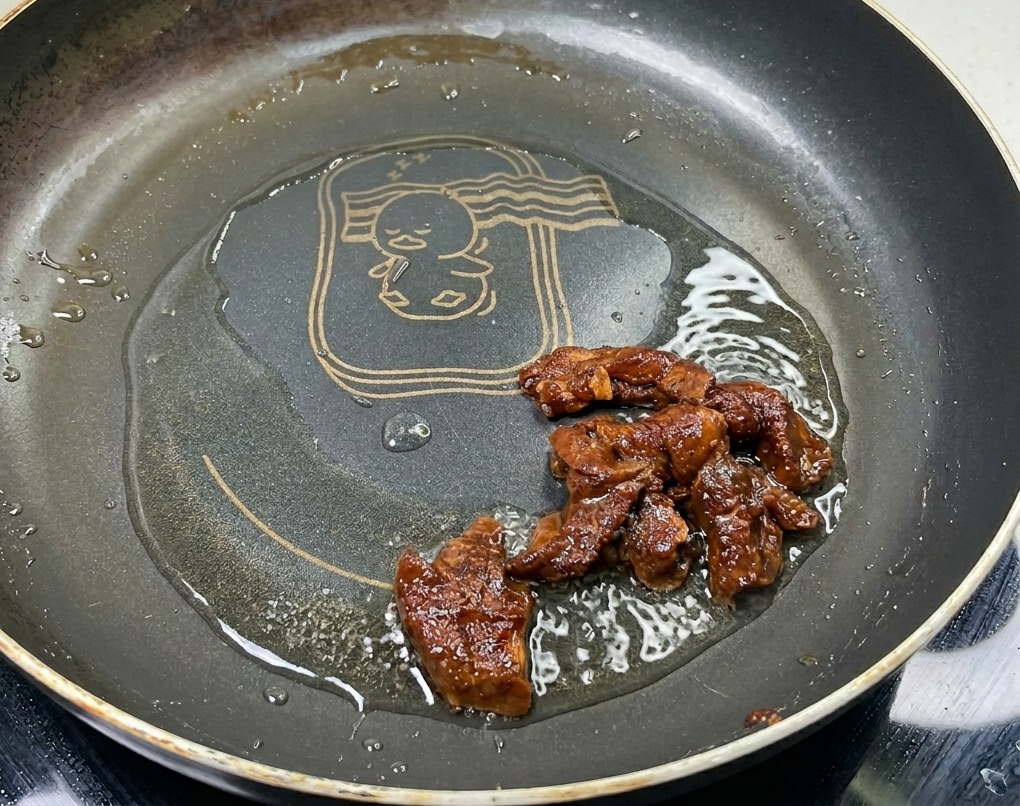 Marinierte Schweinefleischstreifen werden in einer heißen Pfanne mit Öl angebraten und entwickeln eine kräftige, glänzende Bräunung.