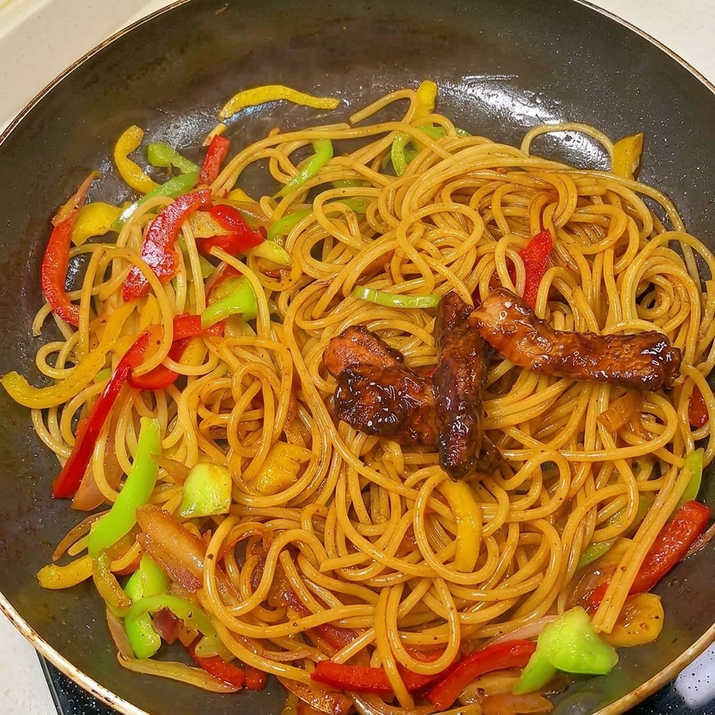 Die fertig angebratenen Schweinefleischstreifen liegen auf der mit Pfeffersauce überzogenen Pasta in der Pfanne.