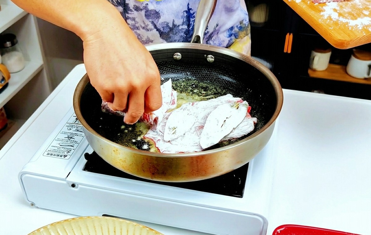 Hände, die leicht mehlierte Kalbfleischscheiben in eine heiße Pfanne mit geschmolzener Butter legen.