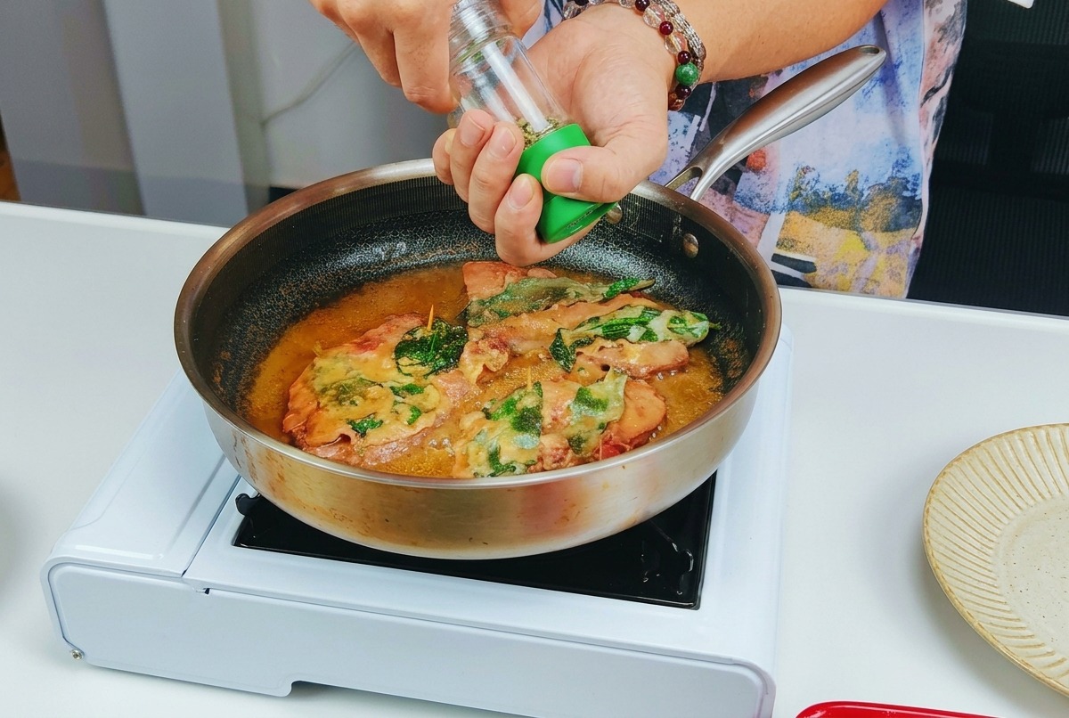 Frischer schwarzer Pfeffer wird aus einer Mühle auf das in der Pfanne gärende Kalbs-Saltimbocca gemahlen.