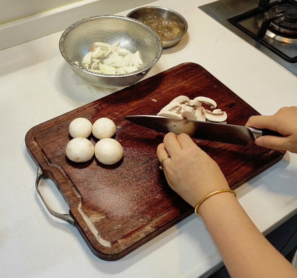 Eine Person schneidet weiße Champignons in dünne Streifen auf einem Holzbrett.