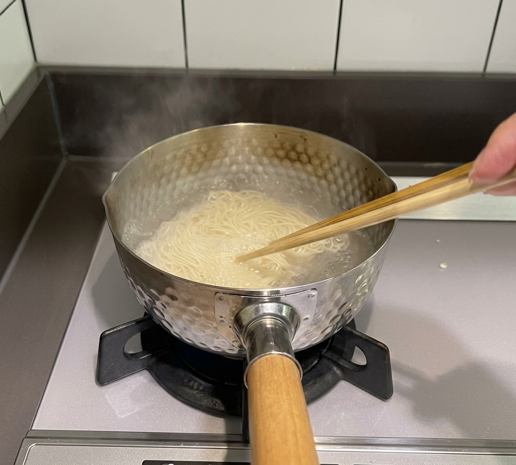 Ein Paar Holzstäbchen rührt dünne Nudeln in einem Topf mit kochendem Wasser auf dem Herd um.