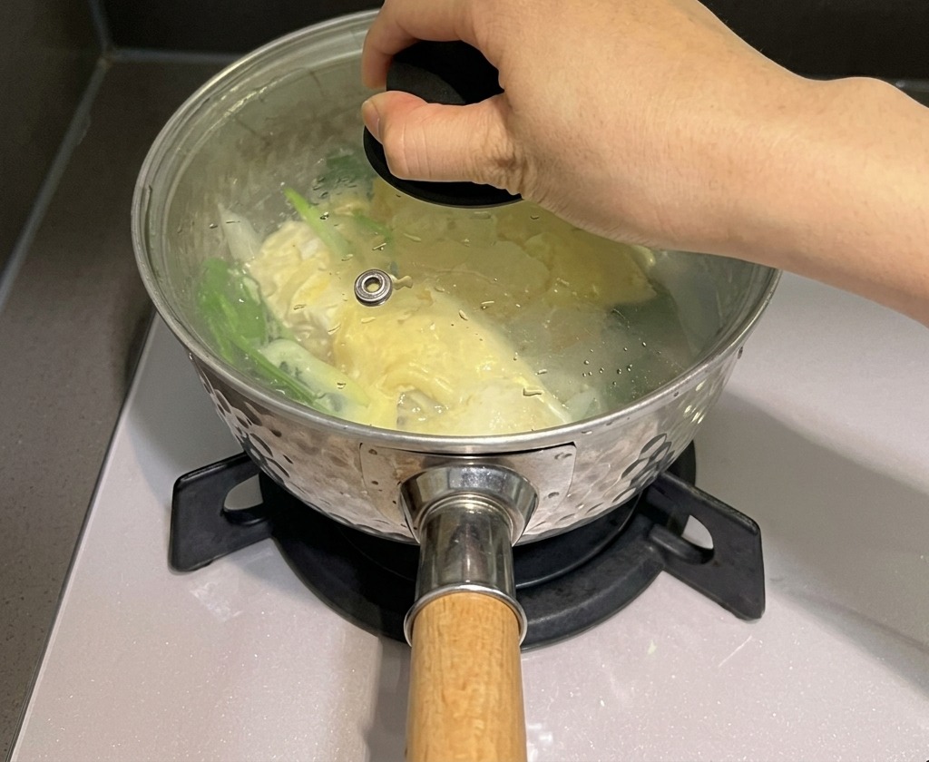 Eine Hand setzt einen Glasdeckel auf einen Topf mit Nudeln und Käse, um den Dampf einzuschließen.