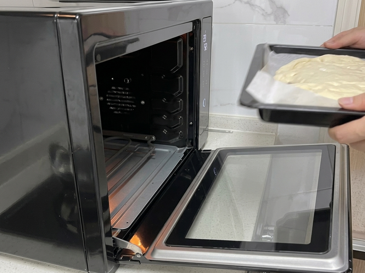 Hände schieben ein Backblech mit Pizzateig in einen offenen schwarzen Ofen.
