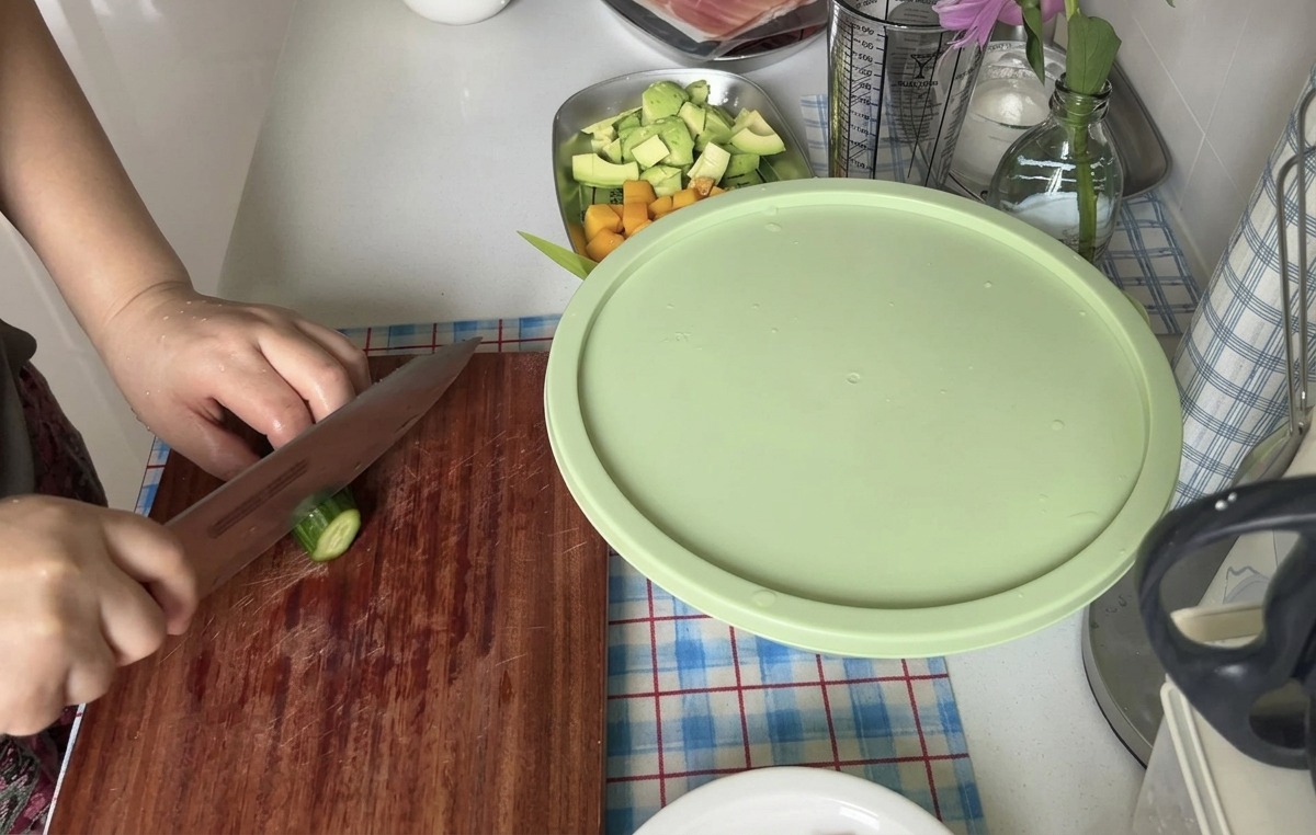 Eine Person schneidet eine frische Gurke mit einem scharfen Messer auf einem Holzbrett in dünne Scheiben.
