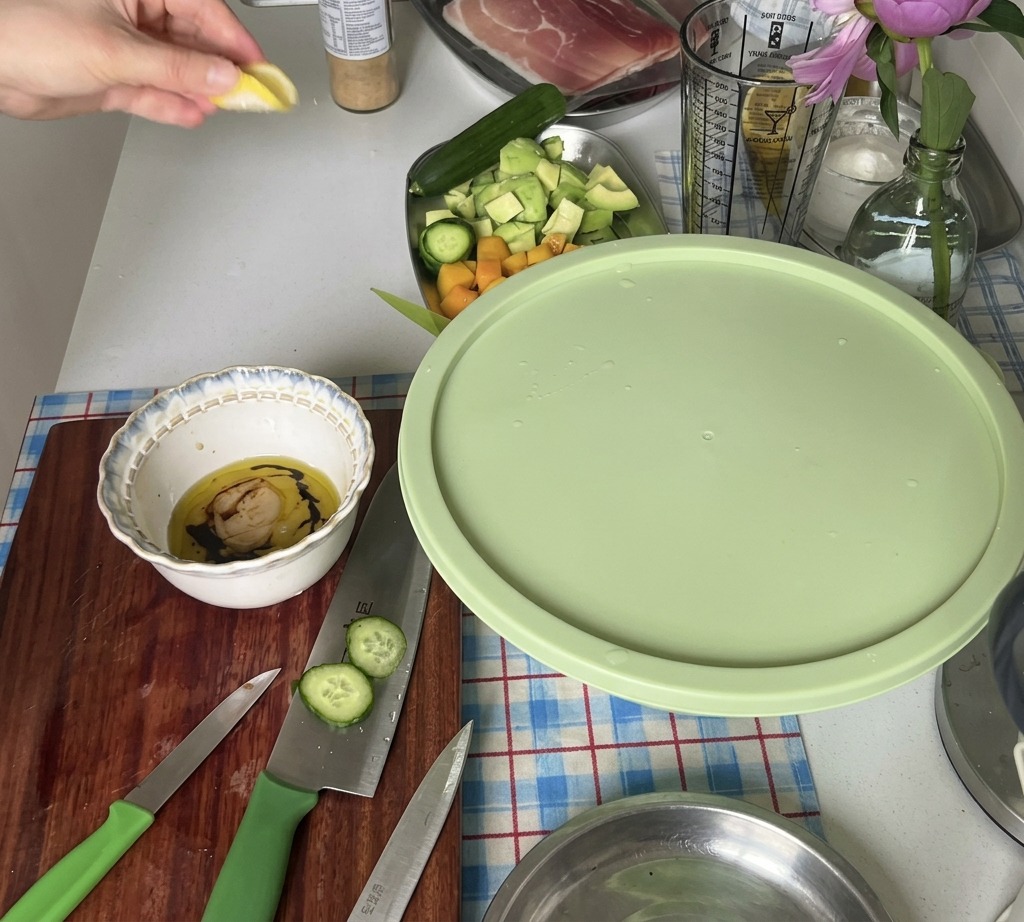 Eine Hand presst den Saft aus einem frischen Zitronenstück in eine kleine Schüssel mit Dressing-Zutaten.