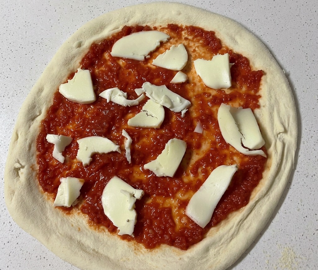 Von Hand gezupfte Stücke aus weißem Mozzarella werden auf der Tomatensauce verteilt.