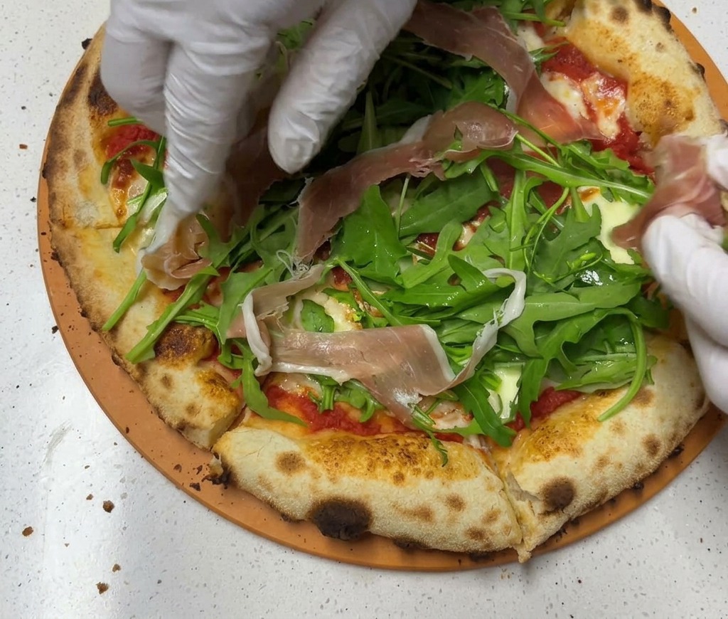 Zarte Scheiben von rosa Parmaschinken werden über dem Rucola auf der Pizza platziert.