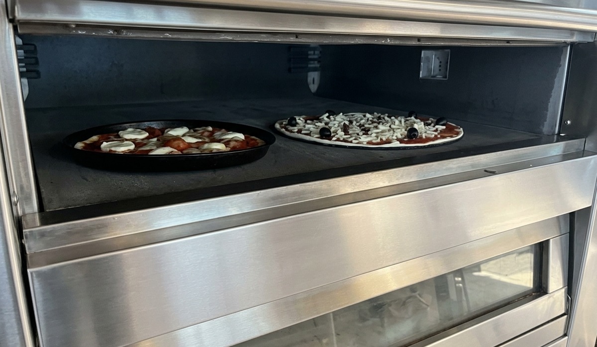 Zwei Pizzas backen auf einer Steinplatte in einem professionellen Deckofen aus Edelstahl.
