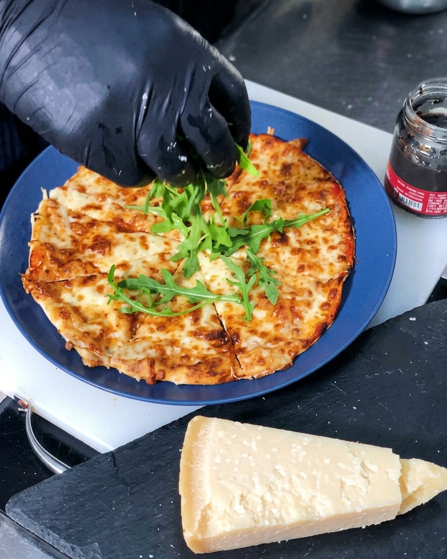 Frische grüne Rucolablätter werden in die Mitte einer geschnittenen, frisch gebackenen Käsepizza gelegt.