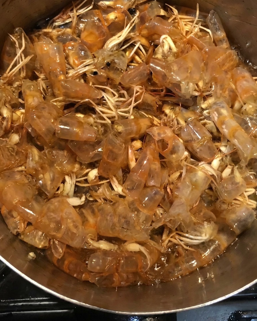 Garnelenschalen köcheln in einer dunklen Saucenmischung im Topf.
