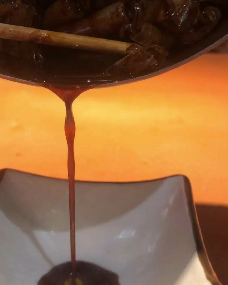 Dunkle, herzhafte Garnelensauce wird durch ein Sieb in eine weiße eckige Schale gegossen.