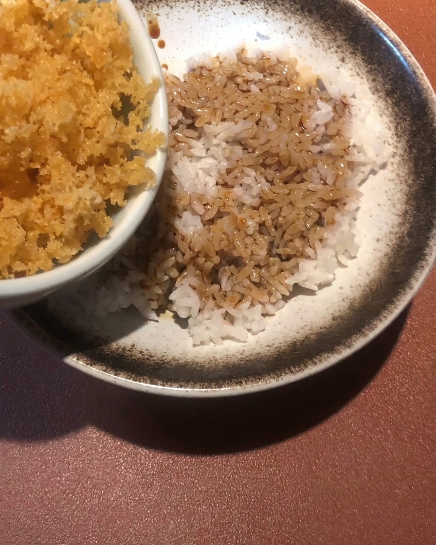 Goldbraune, frittierte Teigkrümel werden über eine Schale mit Reis und Sauce gestreut.