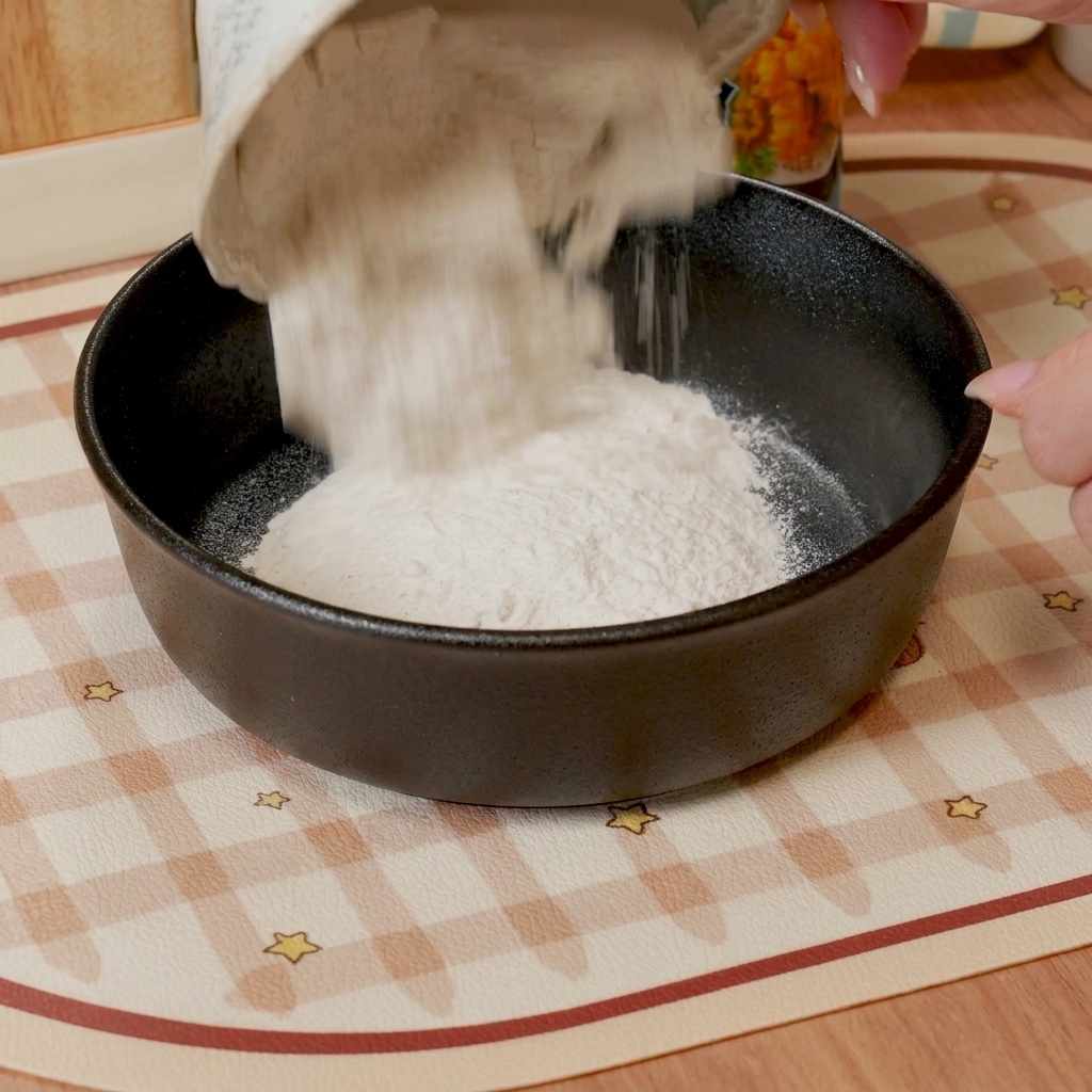 Ein Schneebesen rührt Tempura-Mehl und Wasser in einer dunkel gefärbten Schüssel zu einem glatten, dünnen Teig.