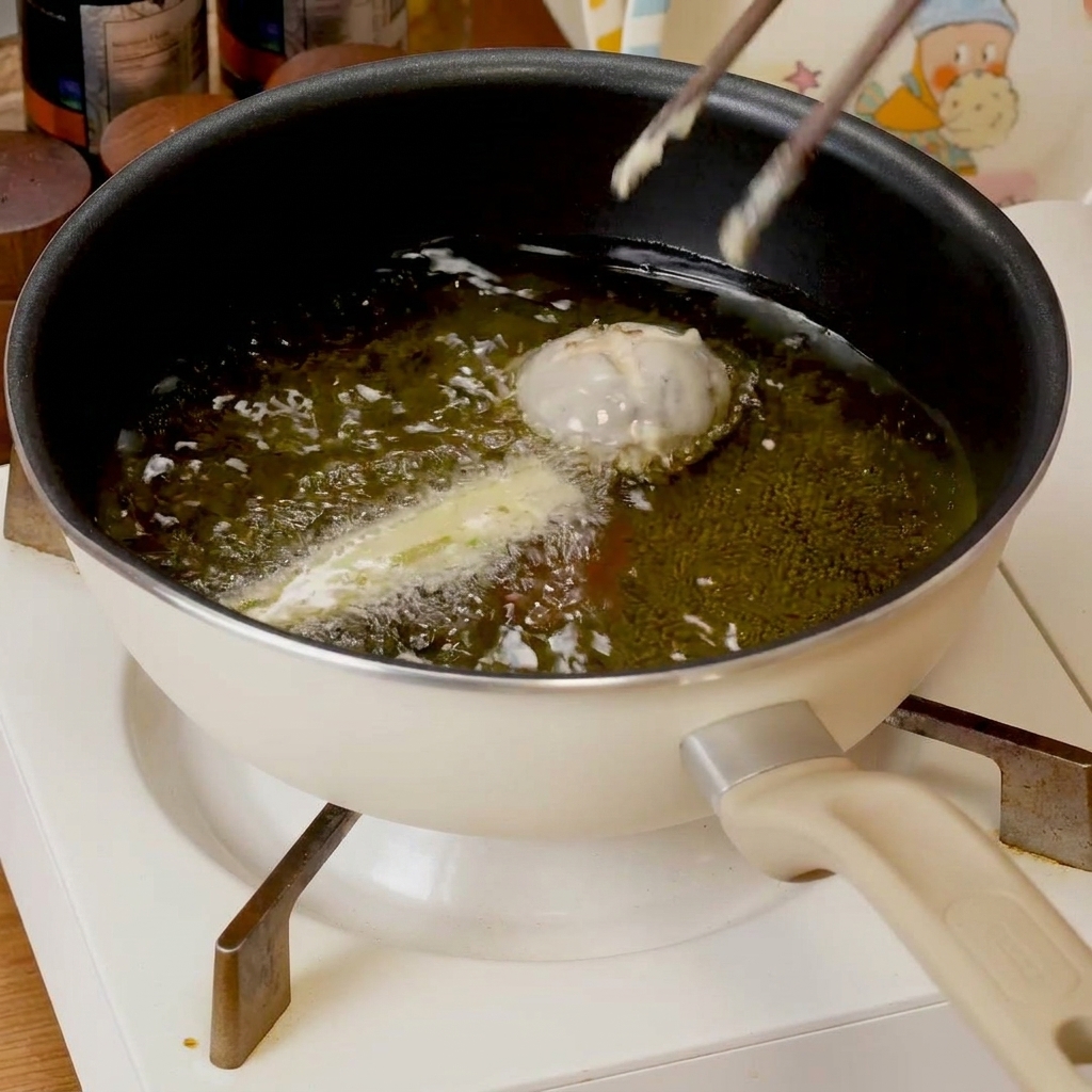 Panierte Tempura-Stücke brutzeln in einer flachen Pfanne mit heißem Öl und werden goldbraun.
