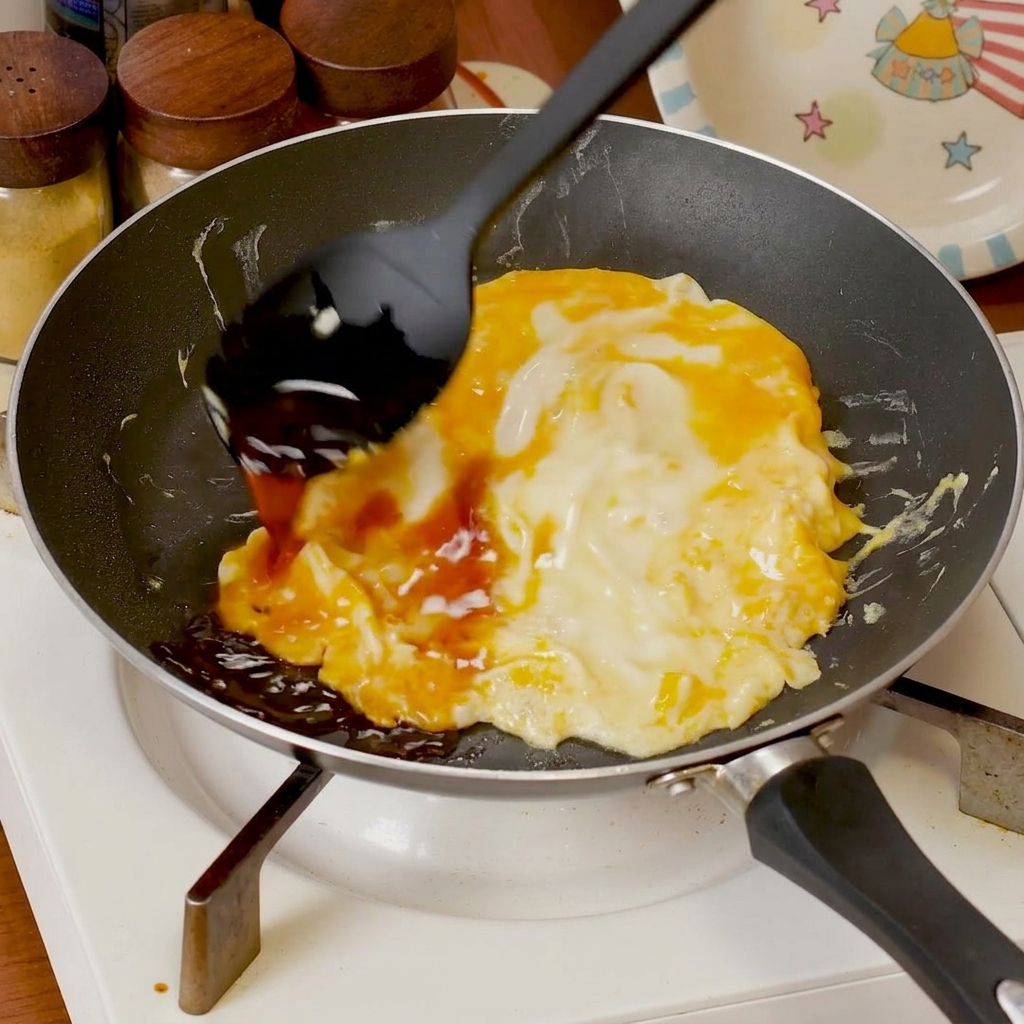 Würzige Sauce wird über in einer Pfanne garendes Rührei gegossen.