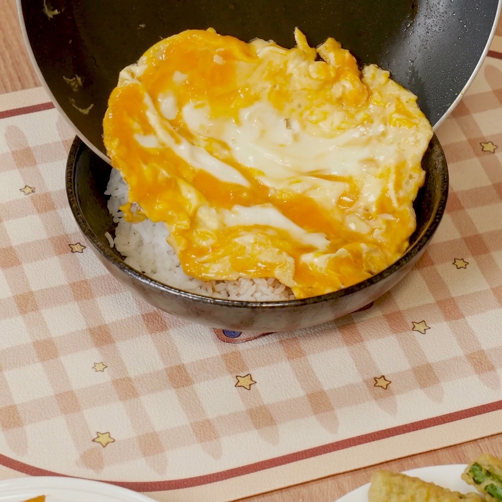 Mit Sauce bedecktes Rührei wird auf eine Schüssel mit weißem Reis geschoben.