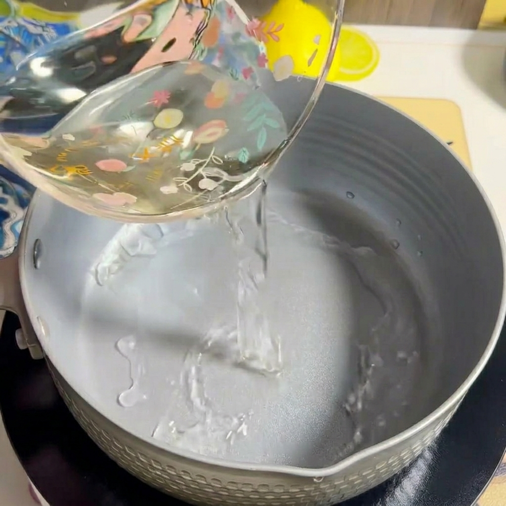 Wasser wird in einen leeren grauen Kochtopf auf einem Herd gegossen.