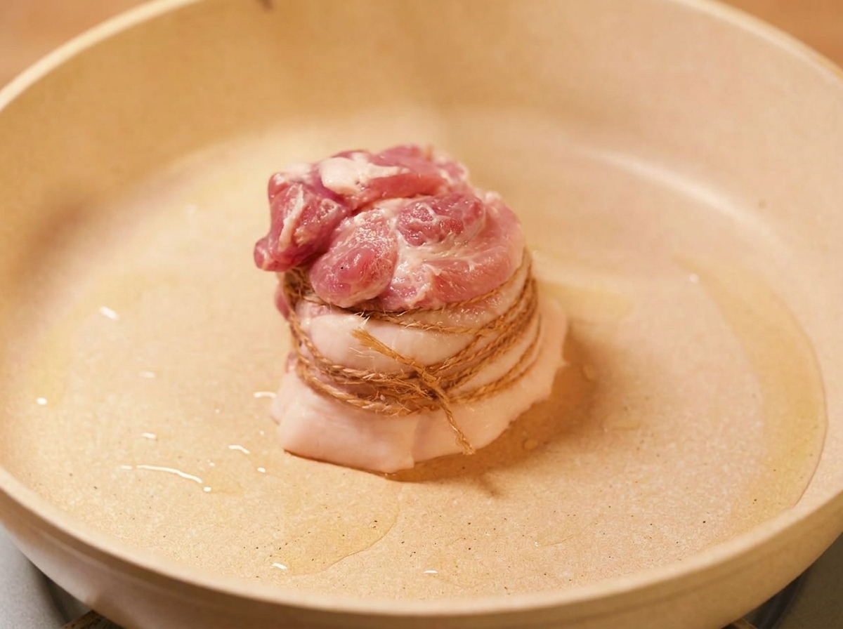 Der verschnürte Schweinebauch wird in einer Pfanne goldbraun angebraten.