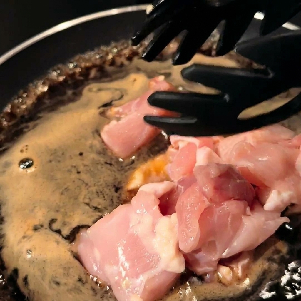 Hähnchenstücke und Zwiebelstreifen werden in der Pfanne mit der Sauce verrührt.
