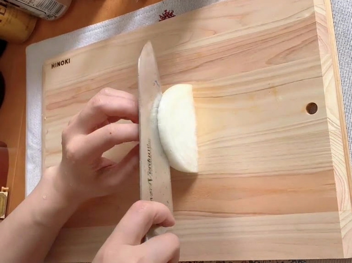 Eine halbe Zwiebel, die auf einem Holzbrett in dünne Streifen geschnitten wird.