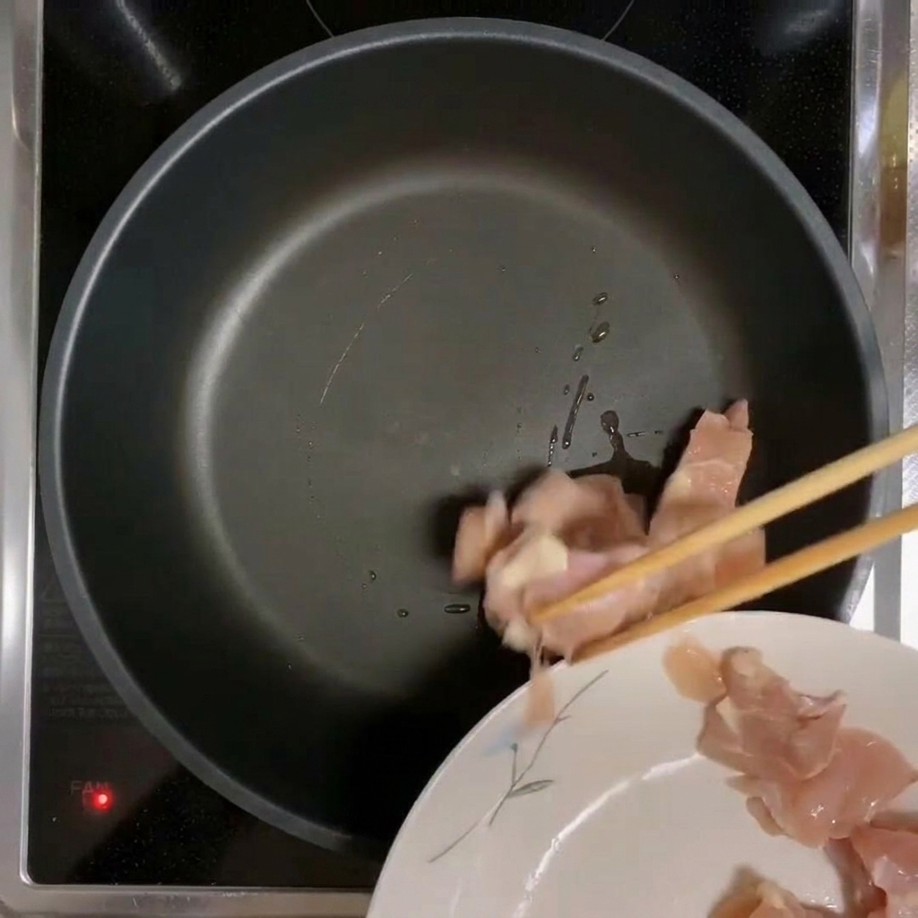 Hähnchenstücke, die in eine vorgeheizte, geölte Pfanne gegeben werden.
