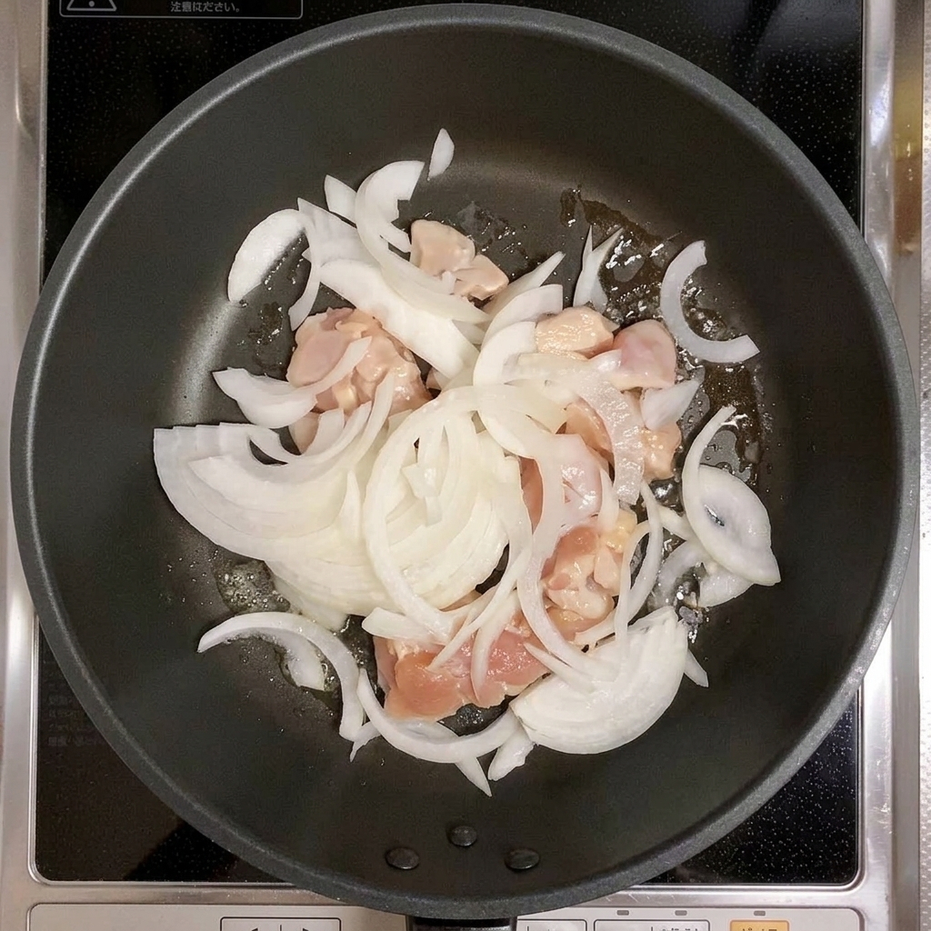 Hähnchen und Zwiebelstreifen, die gemeinsam in einer Pfanne verrührt werden.