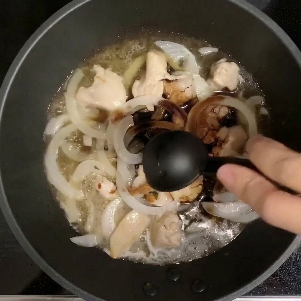 Ein Messlöffel gibt Gewürze in die Pfanne, in der Hähnchen und Zwiebeln in Dashi köcheln.