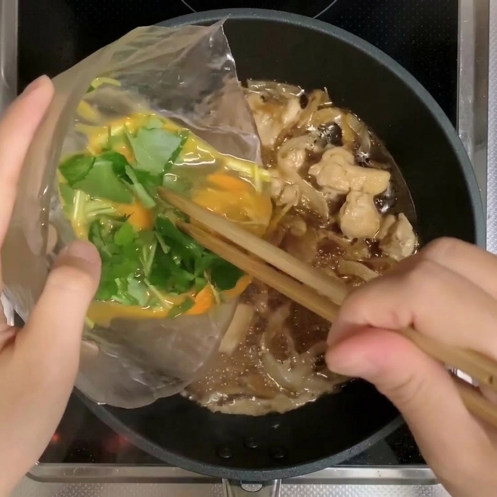 Zwei Drittel der verquirlten Ei-Mitsuba-Mischung werden in die Pfanne zu Hähnchen und Zwiebeln gegossen.