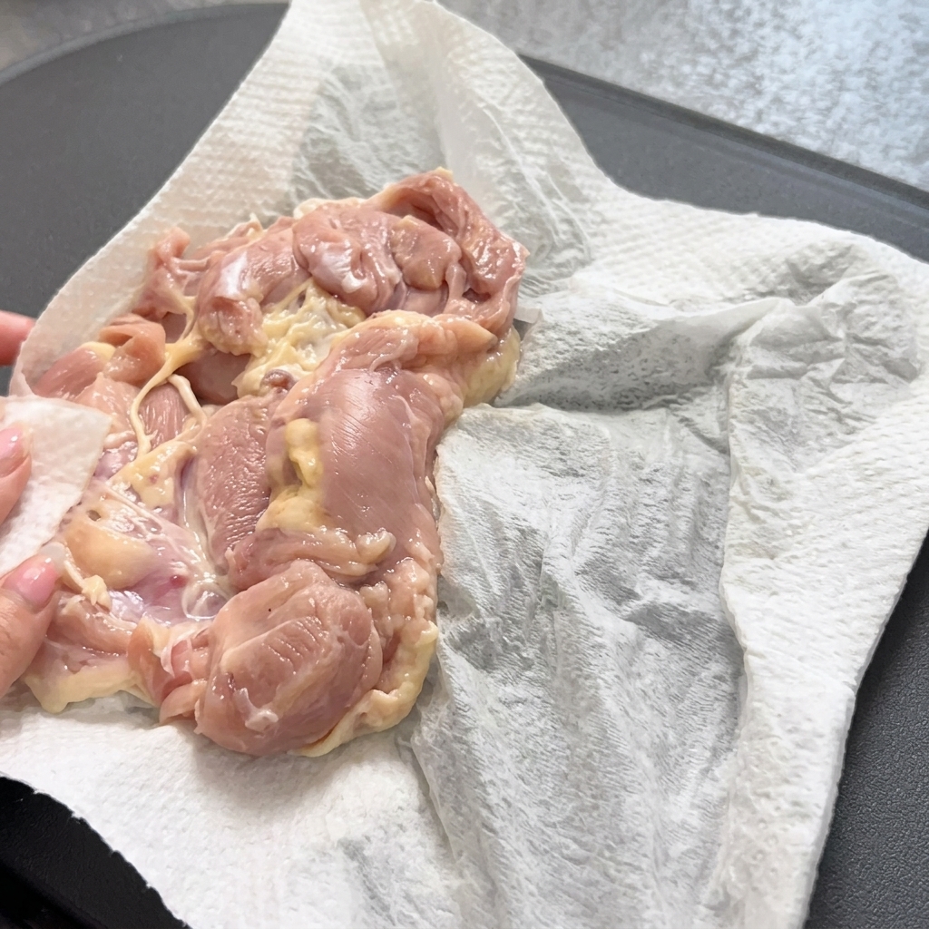 Verwendung einer Zange, um einen rohen Hähnchenschenkel vorsichtig in eine heiße, vorgeheizte Pfanne zu legen.