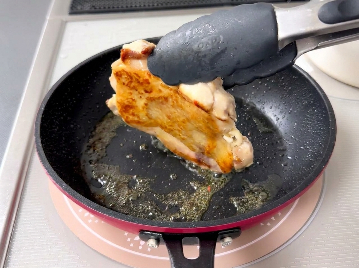 Nahaufnahme einer Zange, die ein Stück Hähnchen wendet, um eine perfekt gebräunte, knusprige Haut zu zeigen.