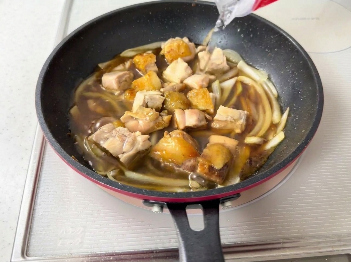 Wasser wird in eine Pfanne mit köchelndem Hähnchen, Zwiebeln und dunkler Sauce gegossen.