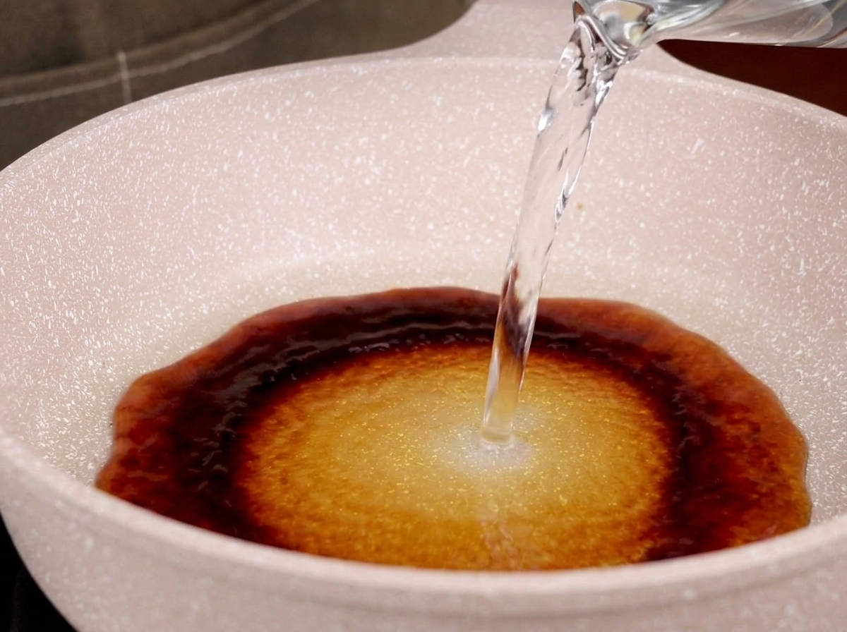 Wasser wird in eine Pfanne mit Teriyaki-Sauce gegossen, wodurch eine Mischung entsteht.