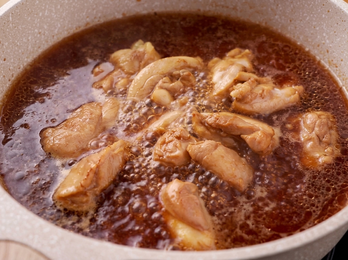Schaum wird von der Oberfläche einer kochenden Hähnchen-Teriyaki-Saucen-Mischung abgeschöpft.