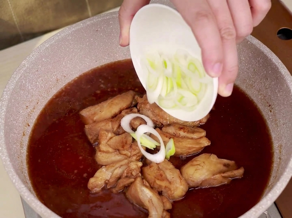 In Scheiben geschnittener Lauch wird in eine Pfanne mit köchelndem Hähnchen und Teriyaki-Sauce gestreut.