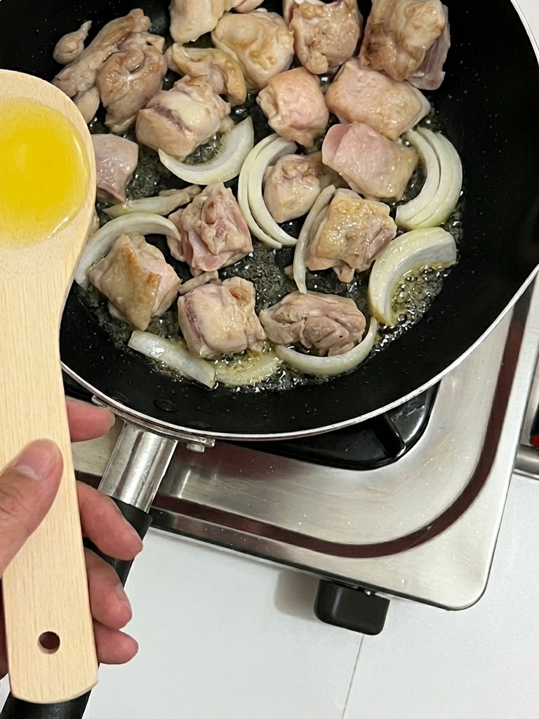 Zwiebelstreifen werden in die Pfanne zu den Hähnchenstücken gegeben.