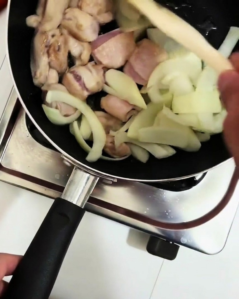 Kochwein wird mit einer Schöpfkelle in die Pfanne zu Hähnchen und Zwiebeln gegeben.