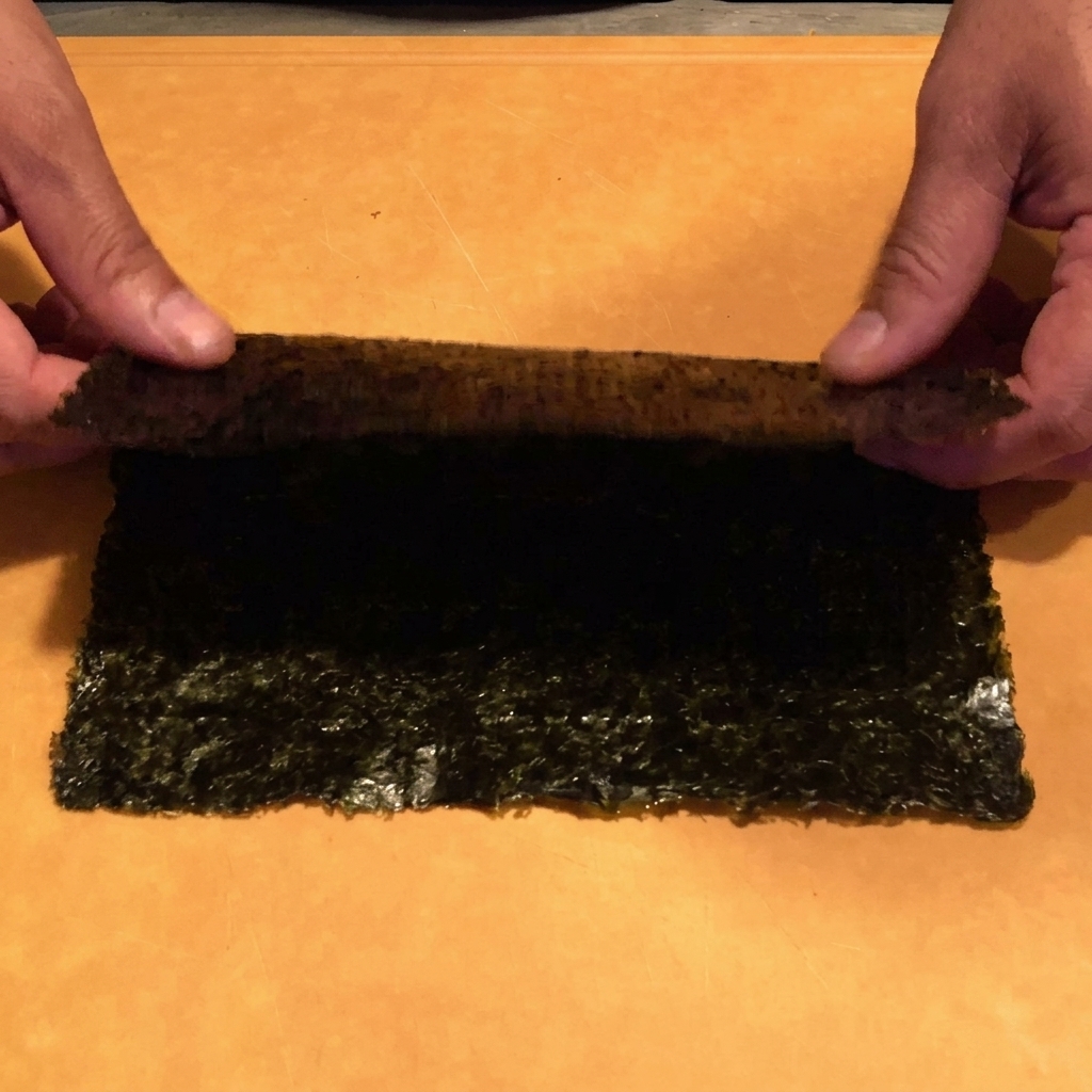 Hände, die mit einer Küchenschere ein Nori-Blatt in feine Streifen über einer Schüssel schneiden.