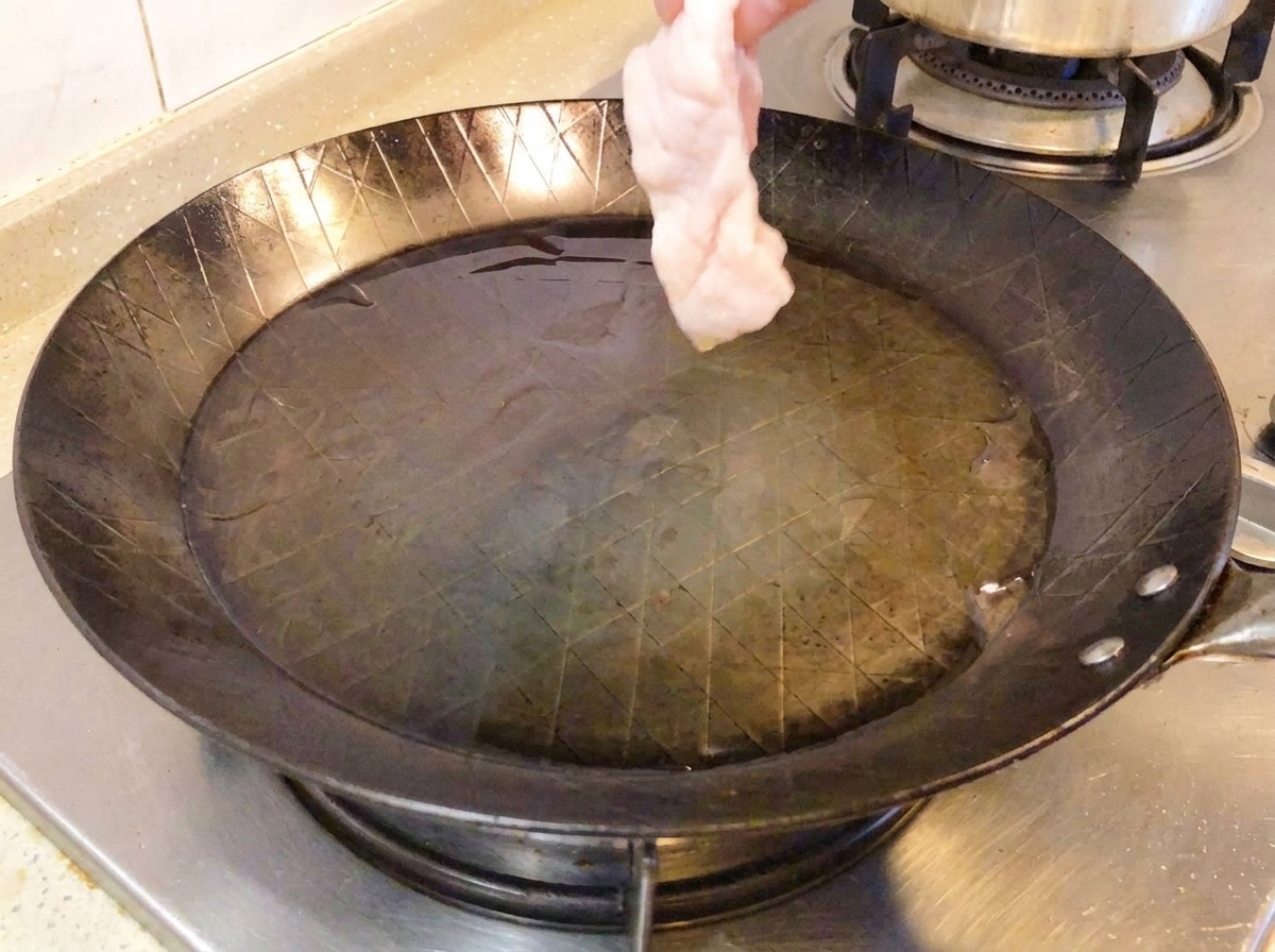 Rohe Hähnchenkeule mit der Haut nach unten in einer heißen Pfanne.