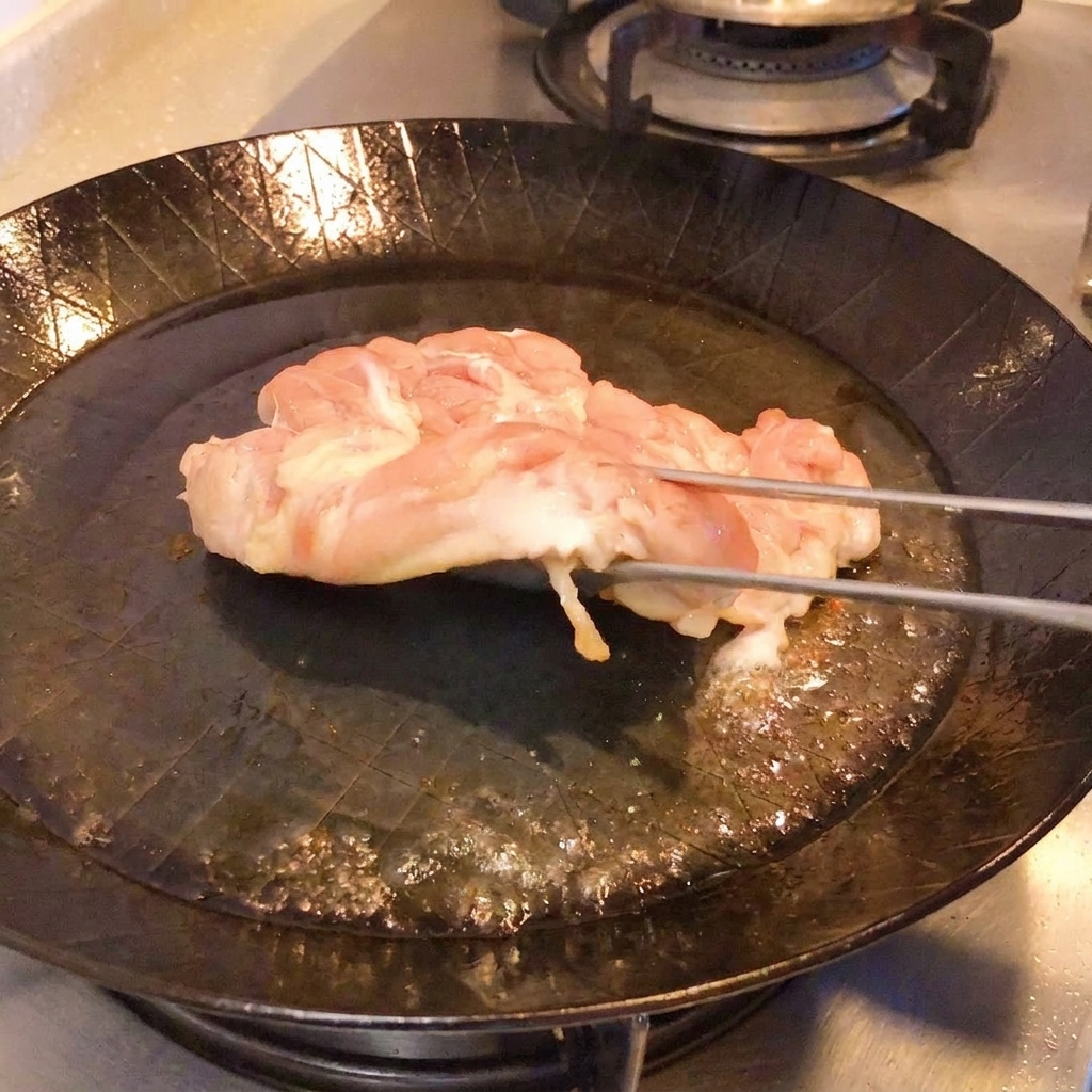 Eine Zange hebt das Hähnchen in der Pfanne an, um die knusprige, goldbraune Haut zu zeigen.