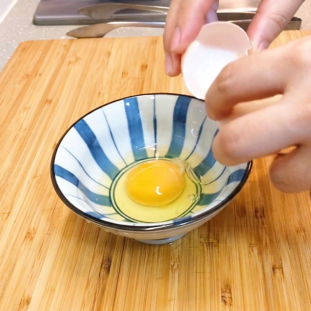 Zwei rohe Eier werden in einer blau-weiß gestreiften Keramikschüssel sanft mit Stäbchen verrührt.