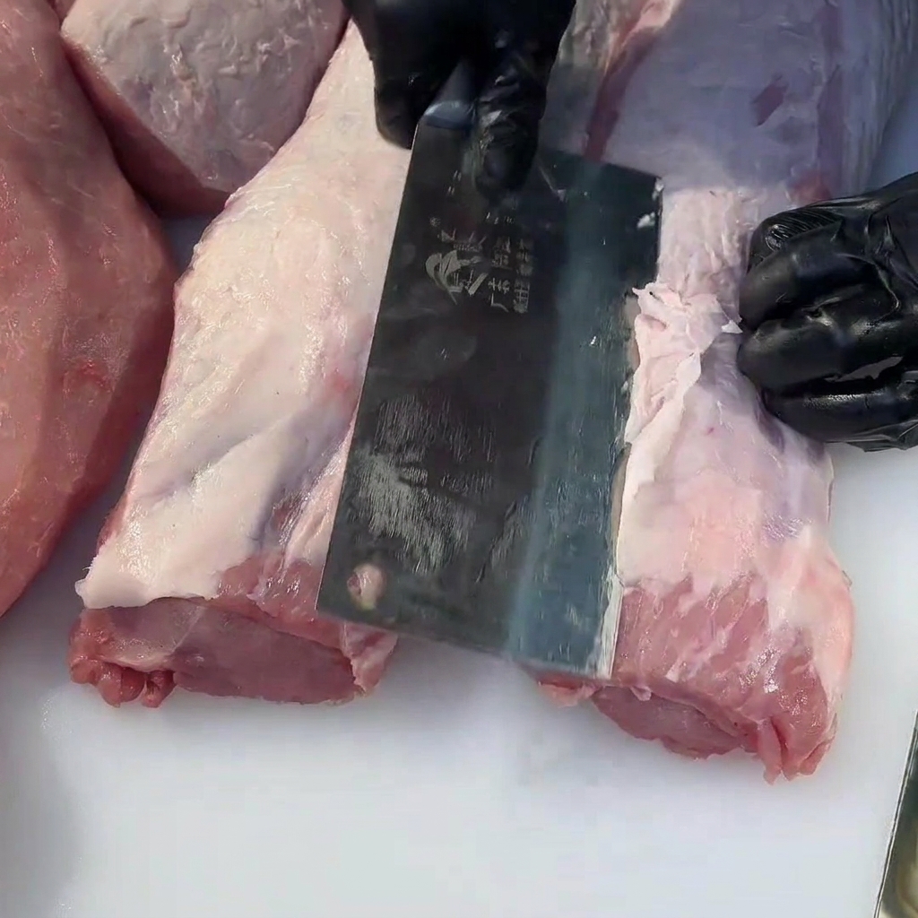 Nahaufnahme eines Fleischbeils, das überschüssiges Fett von einem rohen Schweinefilet entfernt.