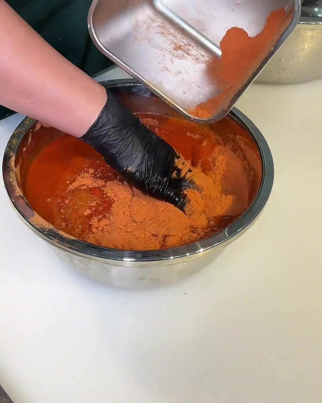 Eine Schüssel mit roter Marinade, in der die Schweinefleischstücke mit einer behandschuhten Hand gewendet werden.