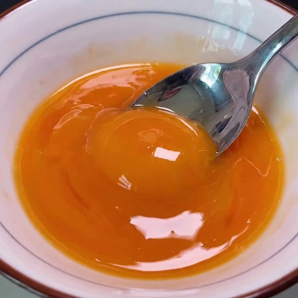 Eine Schüssel mit verquirlten goldenen Eigelben wird über die Kotelett-Zwiebel-Mischung in einer heißen Pfanne gegossen.