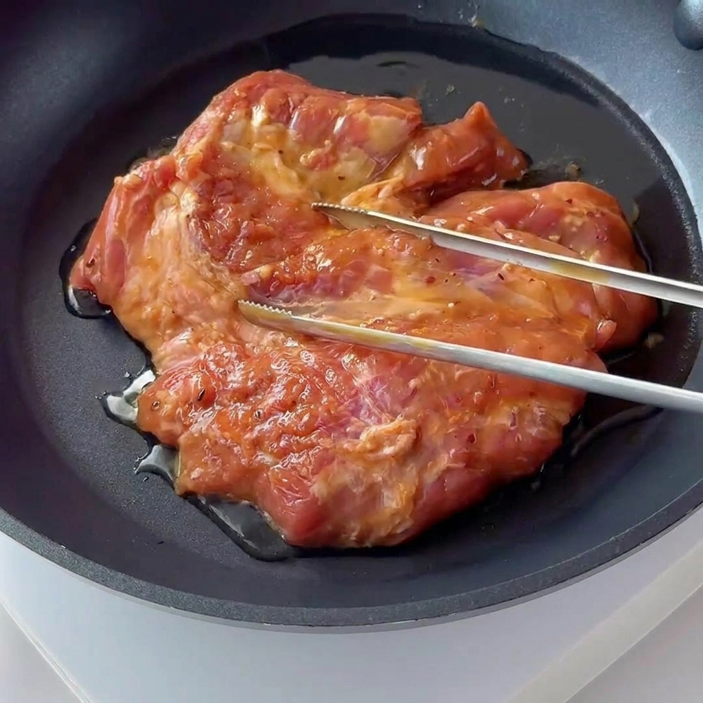 Ein mariniertes Schweinekotelett brutzelt und bräunt in einer dunklen Antihaft-Pfanne.