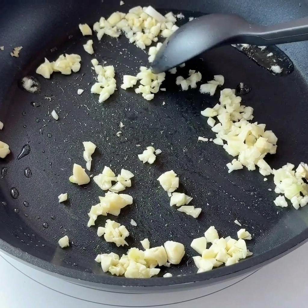 Gehackter Knoblauch und gewürfelte Zwiebeln in einer dunklen Antihaft-Pfanne.